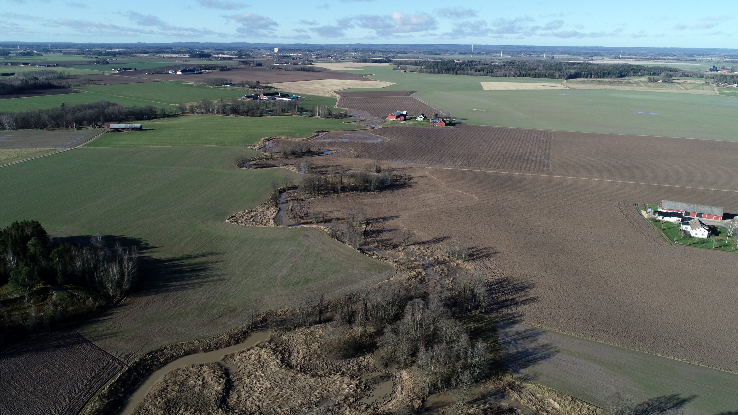 En bild med en å som slingrar sig genom ett jordbrukslandskap